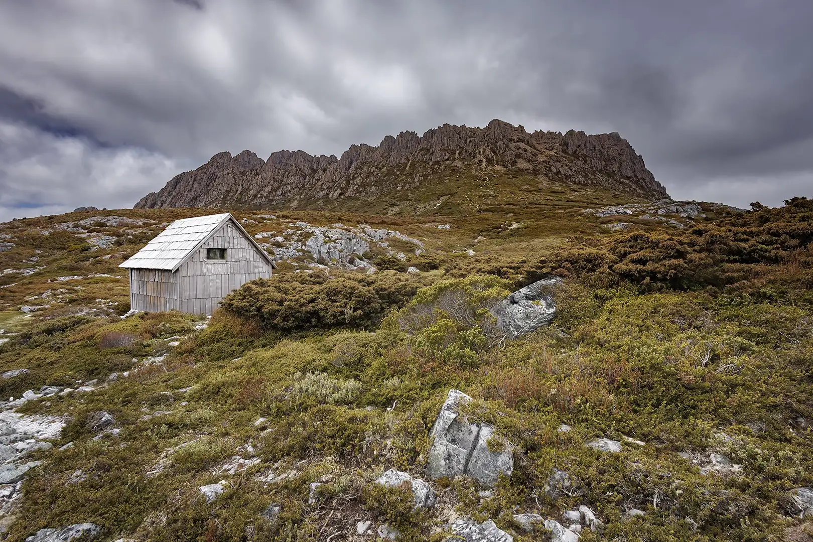 Photo de l'emblématique Kitchen Hut au pied du mont Cradle que l'on peut voir en arrière-plan sous un ciel chargé