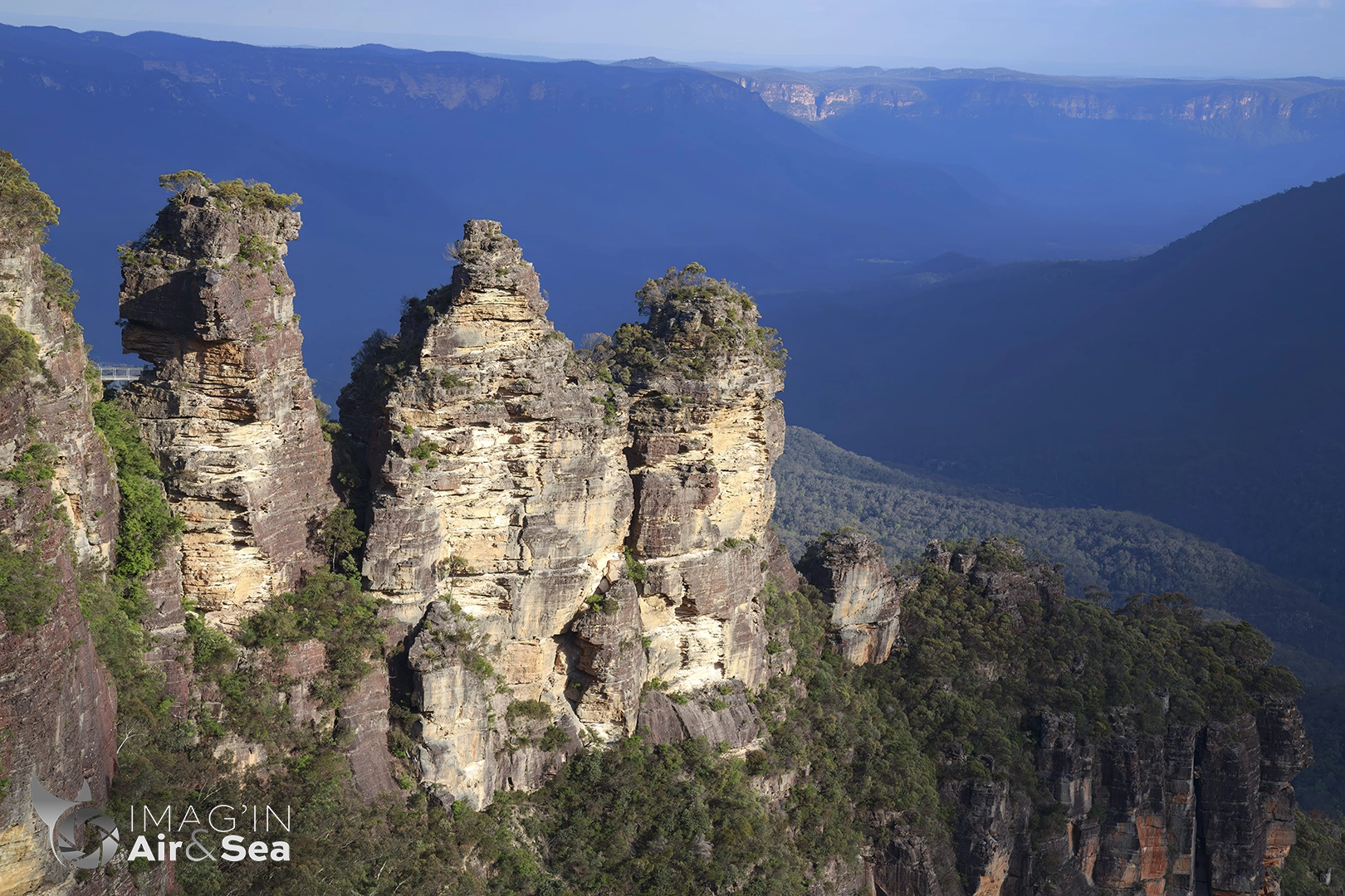 Photo cadrée serrée sur les 3 sisters éclairée par le soleil couchant avec les Blue mountains en arrière plan.
